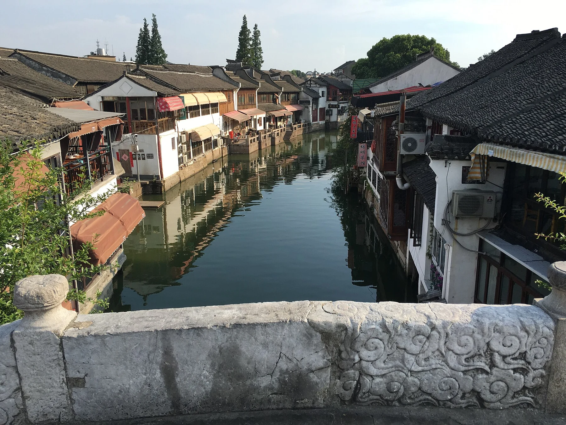 A carved stone rail in the foreground above a canal lined with low tiled roofs.