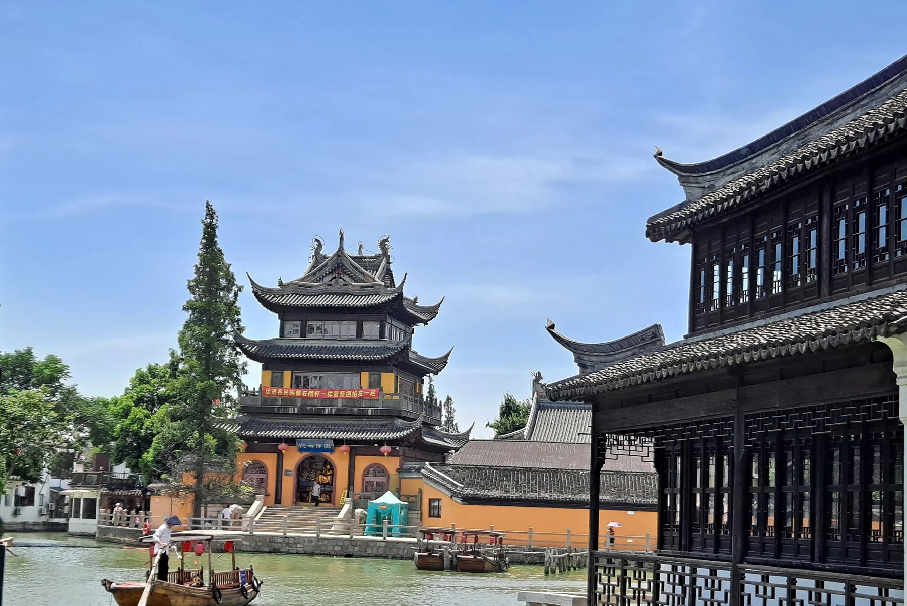 A multi-eaved orange-and-yellow pavilion beside a canal and a long timber-fronted building.